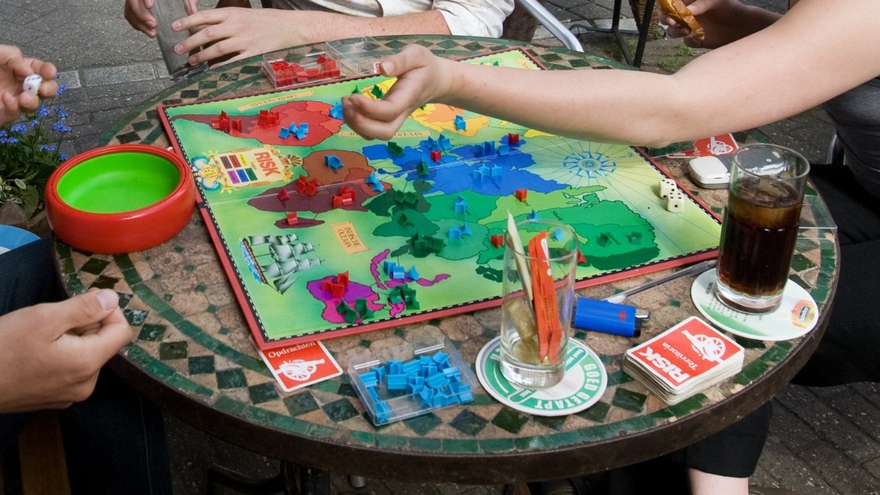 Young group playing RISK in a street cafe. The game board is surrounded by beverages and empty glasses.