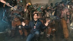 Director Eli Roth holds hands up as he's surrounded by weapon-toting in-character cast members on set of 'Borderlands' (2024).