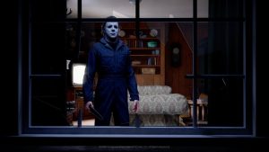 A masked, knife-wielding Michael Myers stares menacingly through a broken living room window (Illfonic's 'Halloween,' 2026)