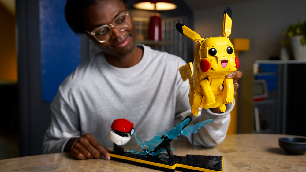 LEGO x Pokemon | Outrun Gaming Promo image for LEGO® Pokemon™ Pikachu and Poke Ball shows person sat at kitchen table examining LEGO Pikachu build. The person is holding Pikachu. | Outrun Gaming