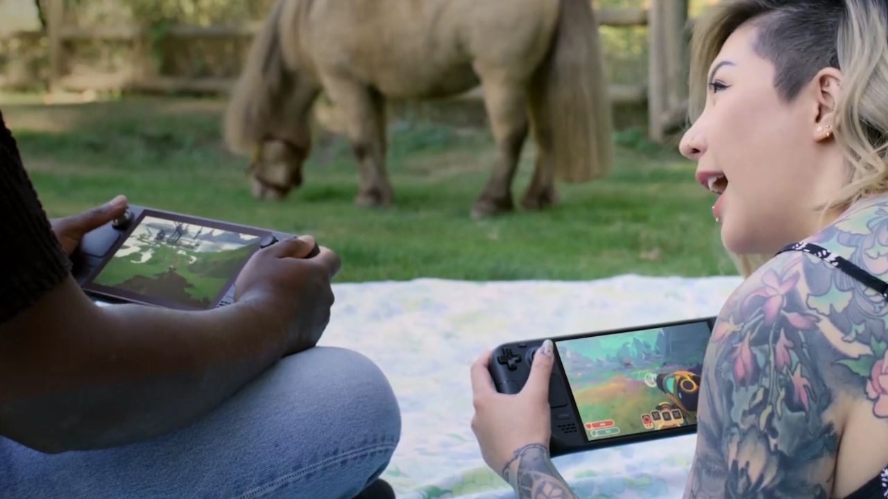 Valve Steam Deck 🎮 Outrun Gaming Two people sit on grass, play Steam Deck handhelds. Person on left turns to friend, smiles 🎮 Outrun Gaming