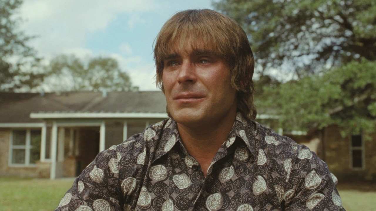 Man with blond hair wearing a paisley shirt sits outdoors in front of a house. 🎮 Outrun Gaming